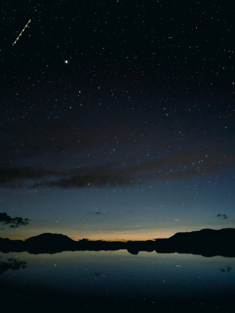 Beautiful silhouette shot of mountains by the river under a starry night sky